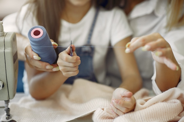 Madre con hija pequeña coser ropa en la fábrica