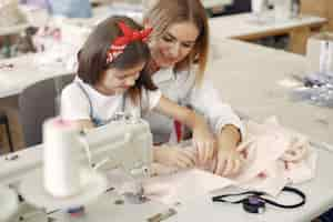 Foto gratuita madre con hija pequeña coser ropa en la fábrica