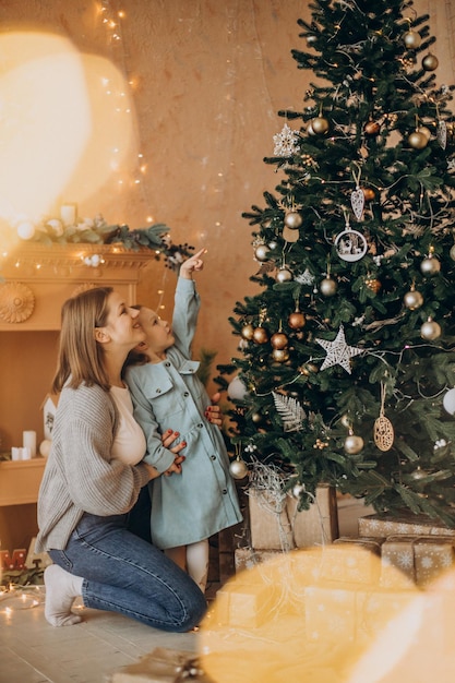 Madre con hija pequeña decorar el árbol de navidad con juguetes