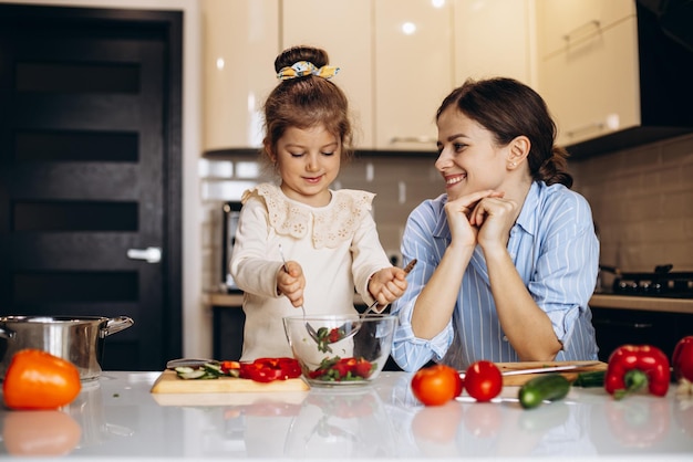 Madre con hija pequeña preparando ensalada