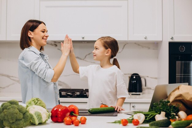 Madre con hija preparando la cena con verduras frescas en la cocina