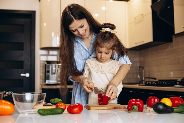 Madre con hija preparando ensalada de verduras frescas en la cocina