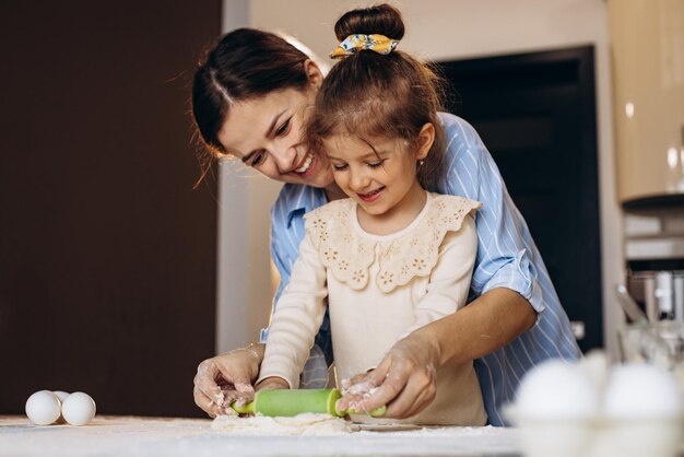 Madre con hija preparando masa usando un molde rodante en la cocina