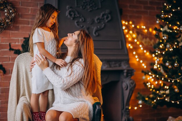 Madre con hija sentada en una silla junto al árbol de navidad