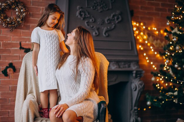 Madre con hija sentada en una silla junto al árbol de navidad