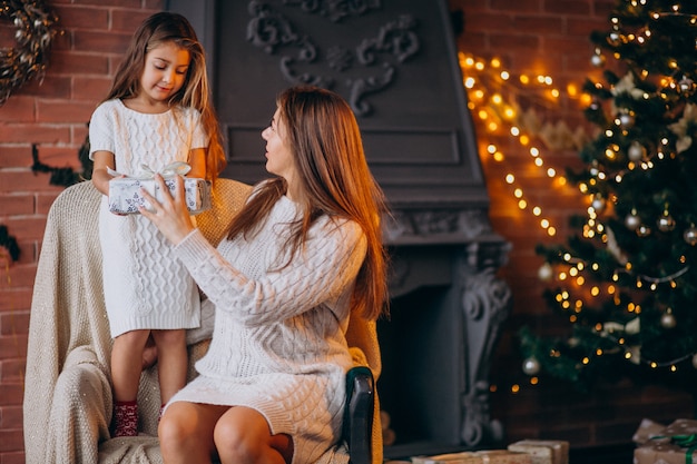 Madre con hija sentada en una silla junto al árbol de navidad