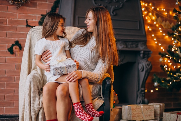 Madre con hija sentada en una silla junto al árbol de navidad