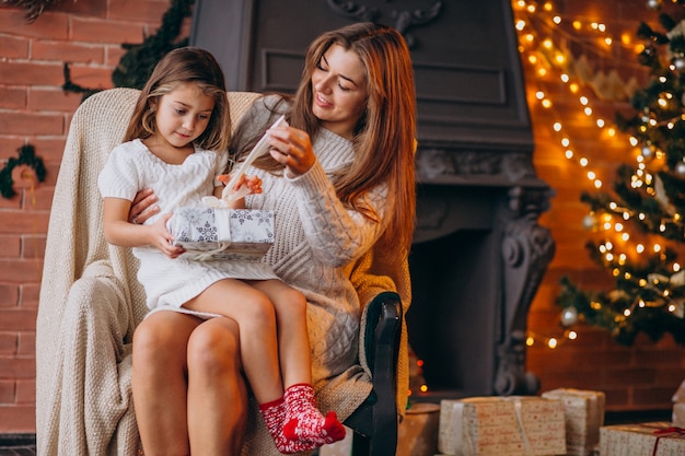 Madre con hija sentada en una silla junto al árbol de navidad