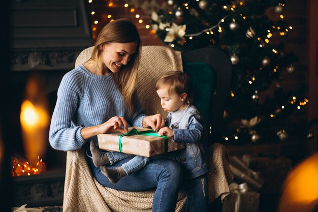 Madre con hija sentada en una silla junto al árbol de navidad