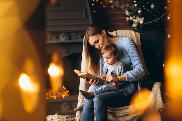 Madre con hija sentada en una silla junto al árbol de navidad