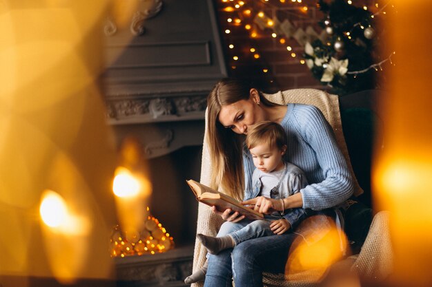 Madre con hija sentada en una silla junto al árbol de navidad