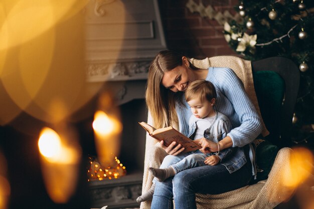 Madre con hija sentada en una silla junto al árbol de navidad