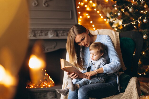 Madre con hija sentada en una silla junto al árbol de navidad