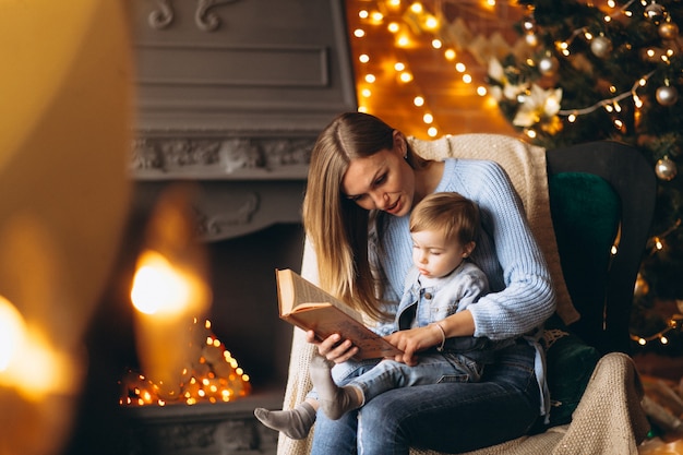 Madre con hija sentada en una silla junto al árbol de navidad