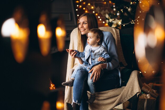 Madre con hija sentada en una silla junto al árbol de navidad