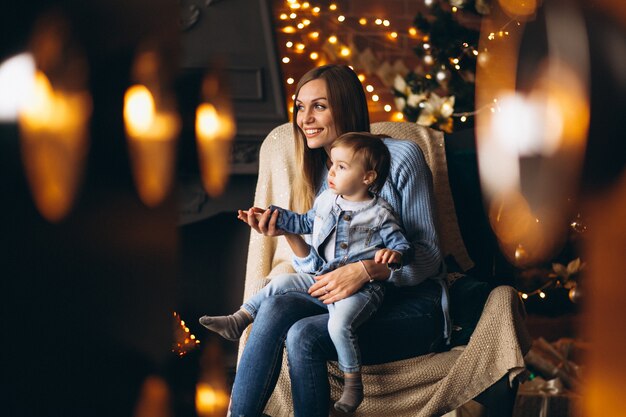 Madre con hija sentada en una silla junto al árbol de navidad