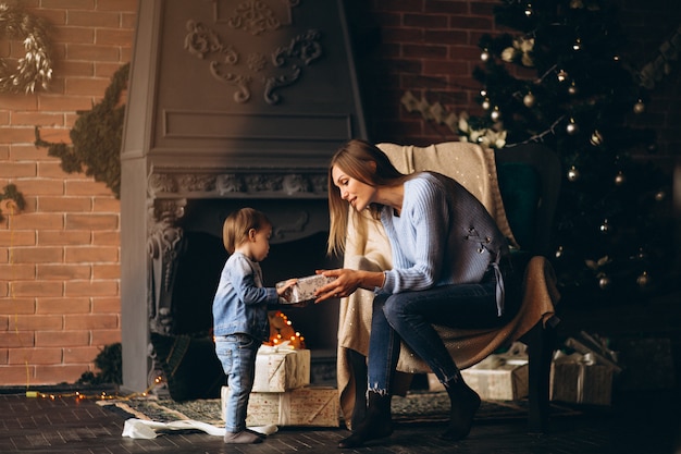 Madre con hija sentada en una silla junto al árbol de navidad