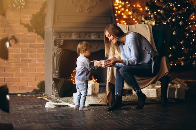 Madre con hija sentada en una silla junto al árbol de navidad