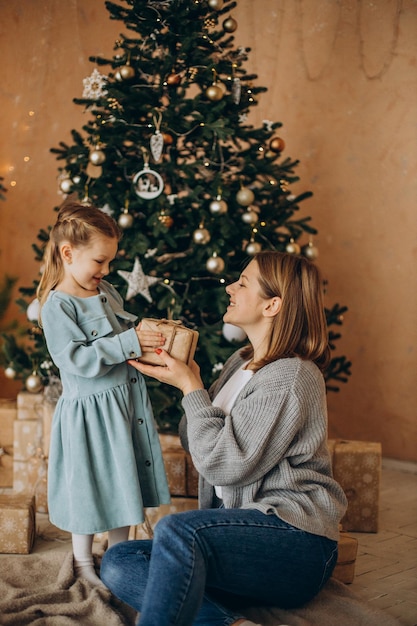 Madre con hija sosteniendo regalos por el árbol de Navidad