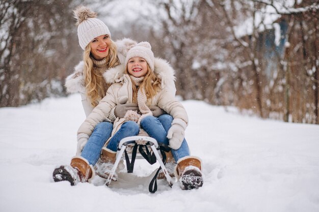 Madre con hija trineo afuera en invierno