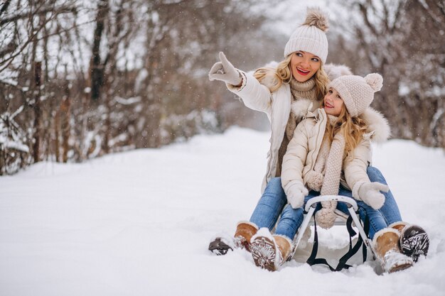 Madre con hija trineo afuera en invierno