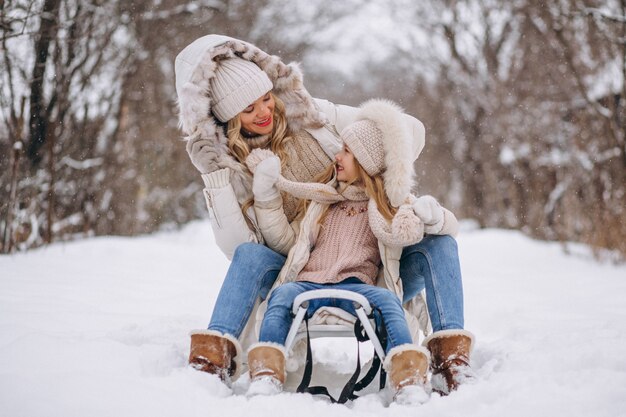 Madre con hija trineo afuera en invierno