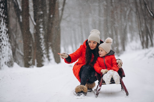 Madre con hija en trineo de parque de invierno