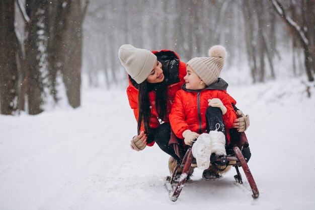 Madre con hija en trineo de parque de invierno