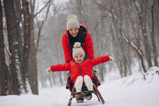 Madre con hija en trineo de parque de invierno