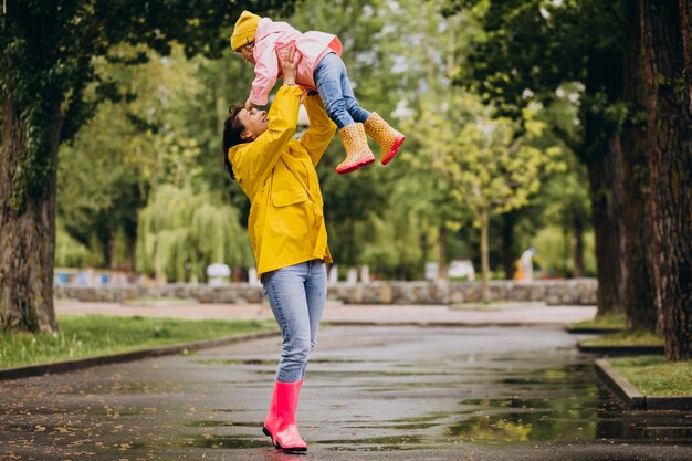 Madre con hija vistiendo abrigo y botas de goma caminando en un clima lluvioso