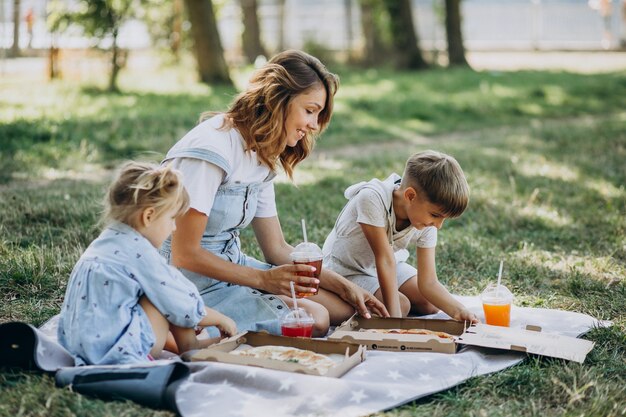 Madre con hijo e hija comiendo pizza en el parque