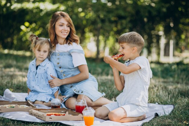 Madre con hijo e hija comiendo pizza en el parque