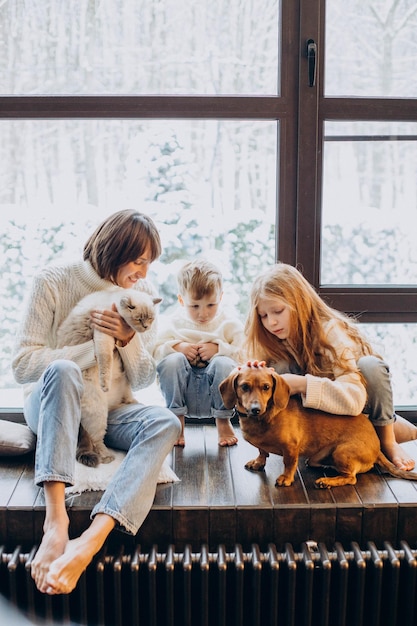 Madre con hijo e hija jugando con su perro en casa junto a la ventana