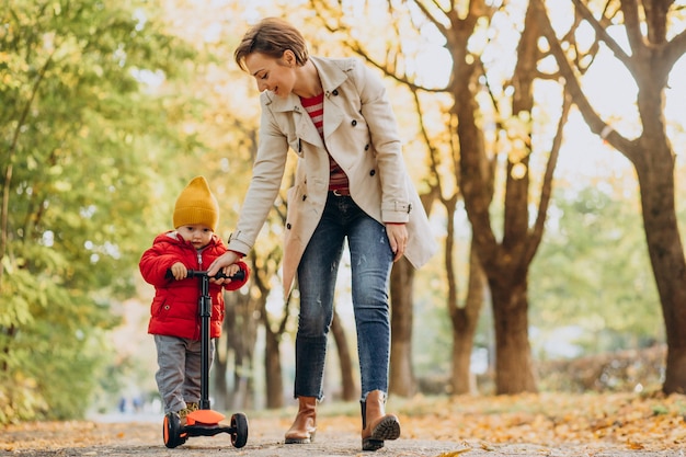 Madre con hijo pequeño en scooter en parque otoñal