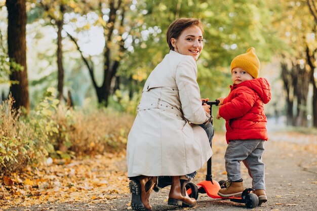 Madre con hijo pequeño en scooter en parque otoñal