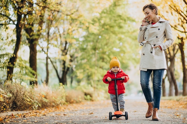 Madre con hijo pequeño en scooter en parque otoñal