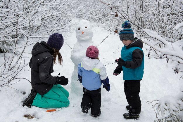 Madre con hijos haciendo muñeco de nieve