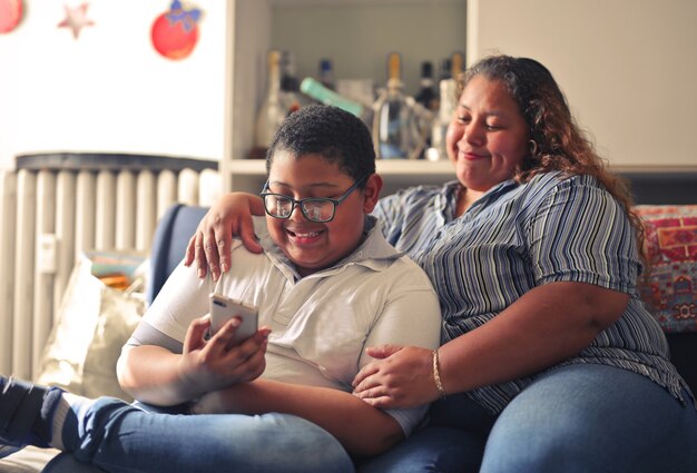 Madre hispana y su hijo trabajando con un teléfono inteligente sentados en el sofá