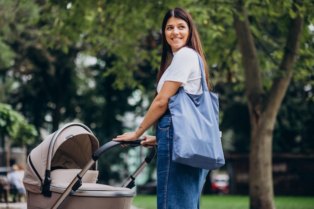 Madre joven caminando con cochecito de bebé en el parque