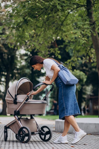 Madre joven caminando con cochecito de bebé en el parque