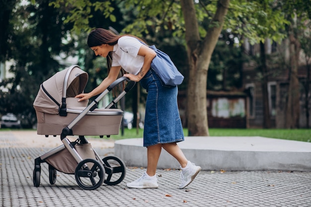 Madre joven caminando con cochecito de bebé en el parque