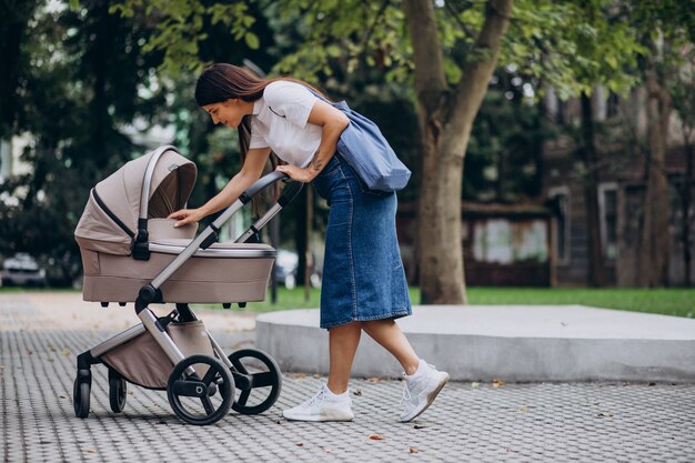 Madre joven caminando con cochecito de bebé en el parque