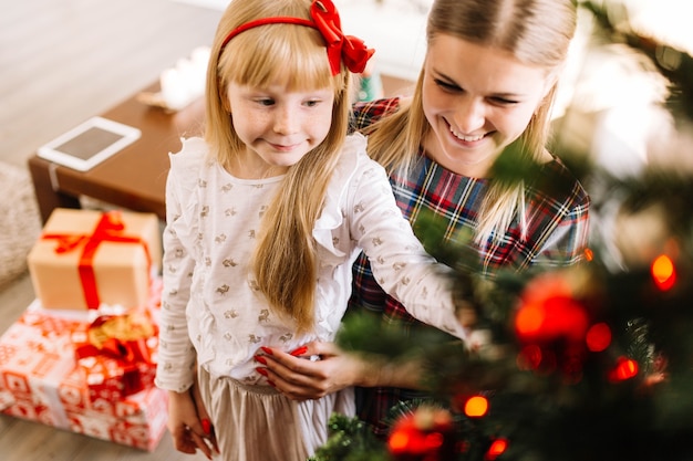 Madre joven e hija decorando árbol de navidad