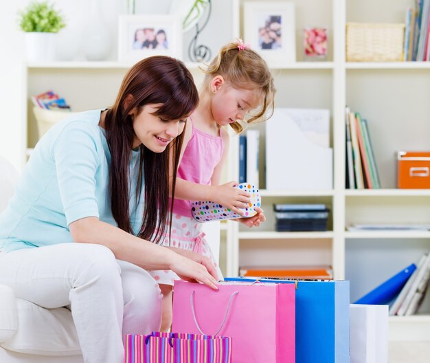 Madre joven con hija pequeña en casa con compras - interiores