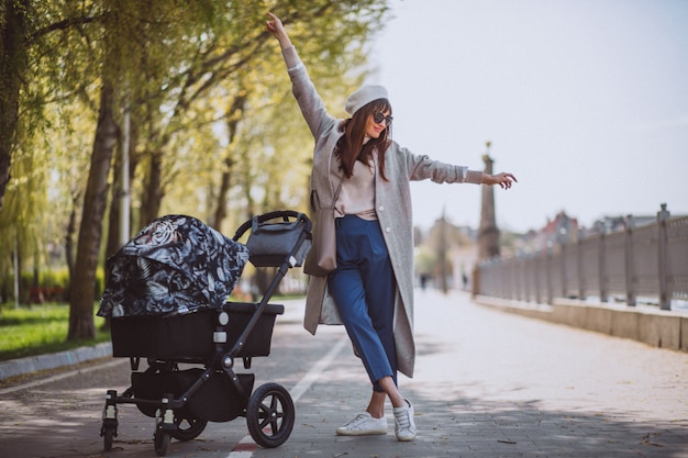 Madre joven que camina con el carro de bebé en parque