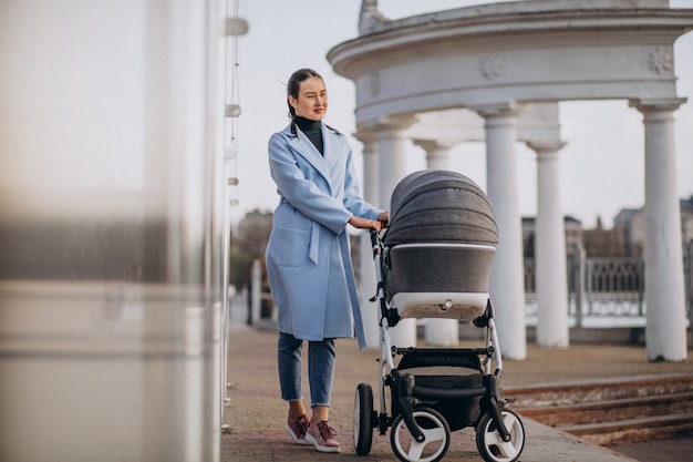 Madre joven que camina con el carro de bebé en parque
