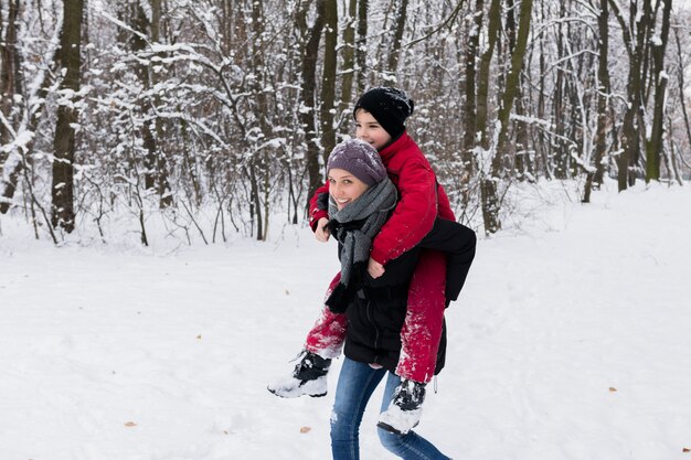 Madre joven que da a cuestas en el bosque en un día de invierno