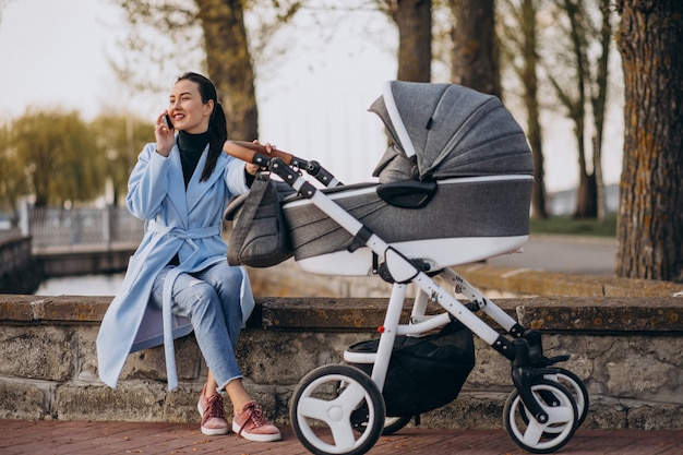 Madre joven que se sienta con el carro de bebé en parque
