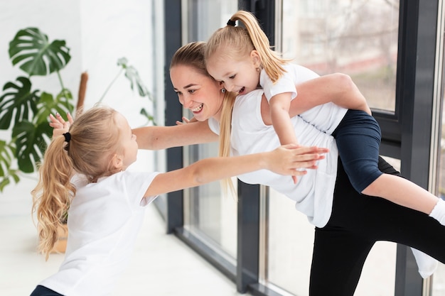 Madre jugando con hijas en casa mientras hace ejercicio