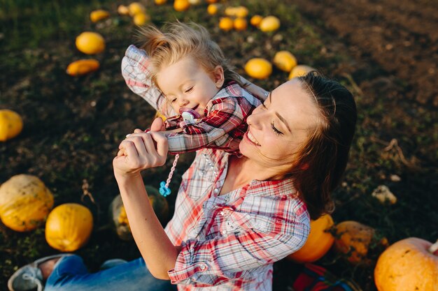 Madre jugando con su hija en un campo con calabazas, víspera de Halloween